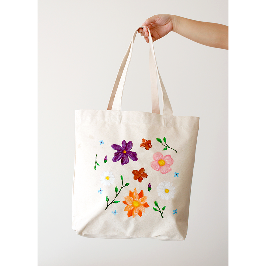 A variety of colourful flowers and leaves hand-painted on a cotton natural beige canvas bag