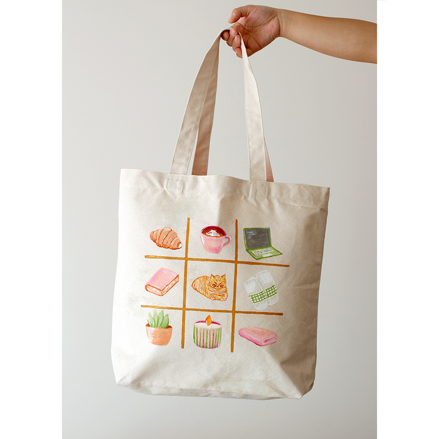A variety of cosy items and a orange tabby cat in feminine colours , on a cotton canvas bag