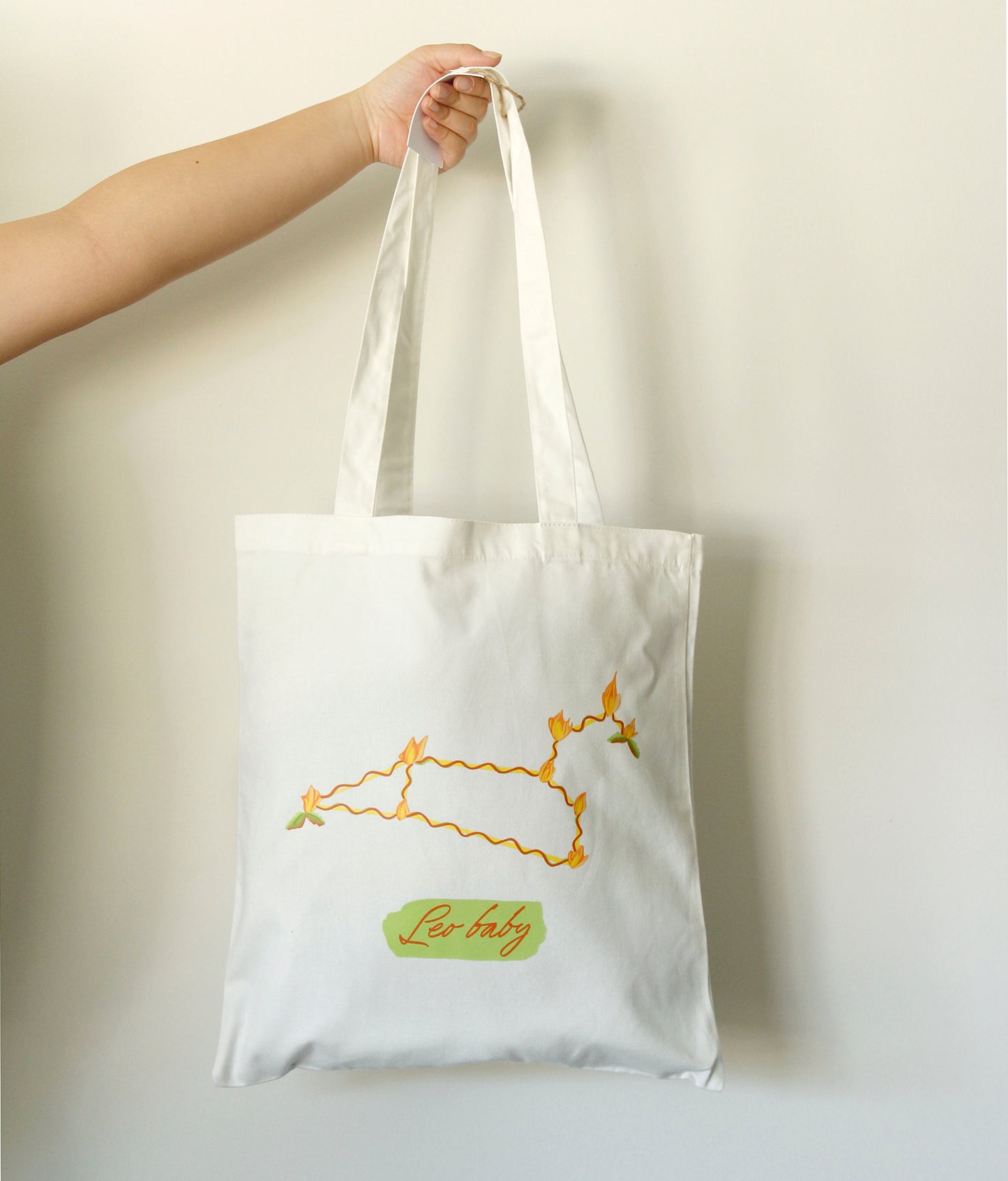 Tote bag with colourful Leo zodiac sign held by a hand against a neutral background