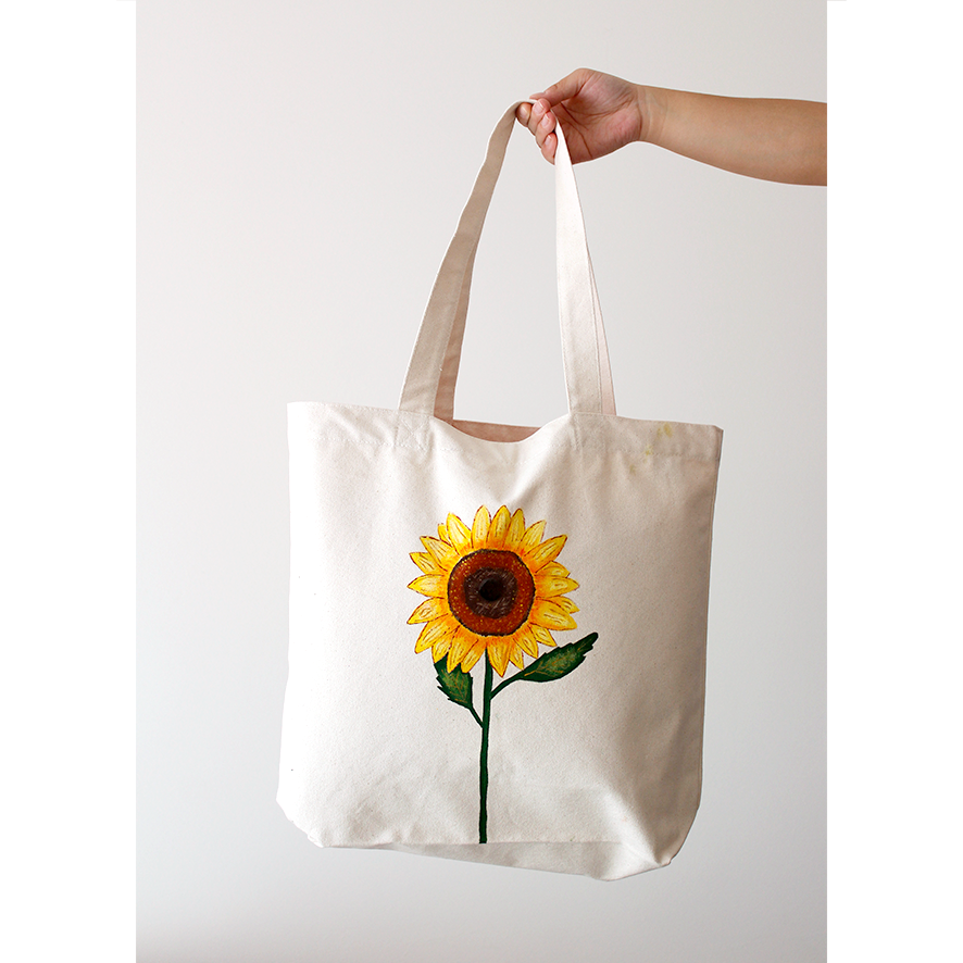 A bright yellow sunflower hand-painted on a natural beige cotton canvas bag