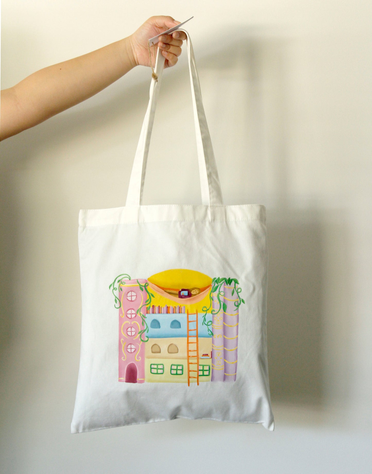 Tote bag with a colorful house made of books design held by a hand against a plain background