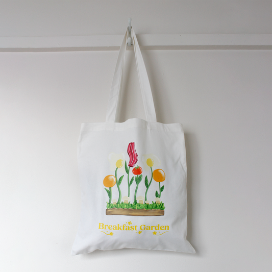 White tote bag with floral/breakfast hybrid design and 'Breakfast Garden' text on a white background
