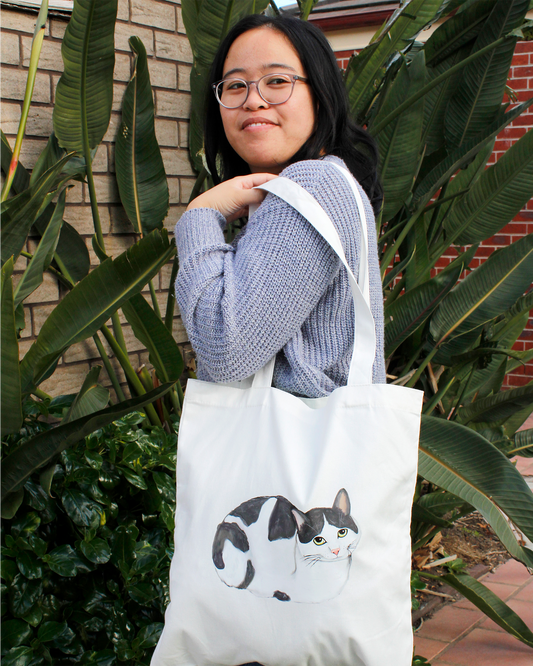 Person holding a tote bag with a cat design outdoors