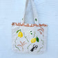 Photo of a hand-painted thick canvased tote bag for sale with vibrant yellow lemons, hand-painted wheat branches, vanilla and terracotta tiles painted on the border of the bag near the handles.