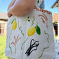 Photo of a hand-painted thick canvased tote bag for sale with vibrant yellow lemons, hand-painted wheat branches, vanilla and terracotta tiles painted on the border of the bag near the handles.