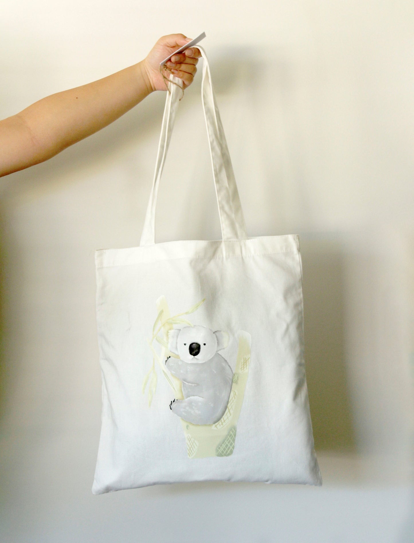 Tote bag with a koala design held by a hand against a plain background