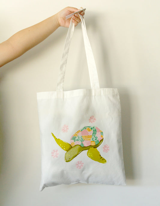 Tote bag with a turtle design held by a hand against a plain background