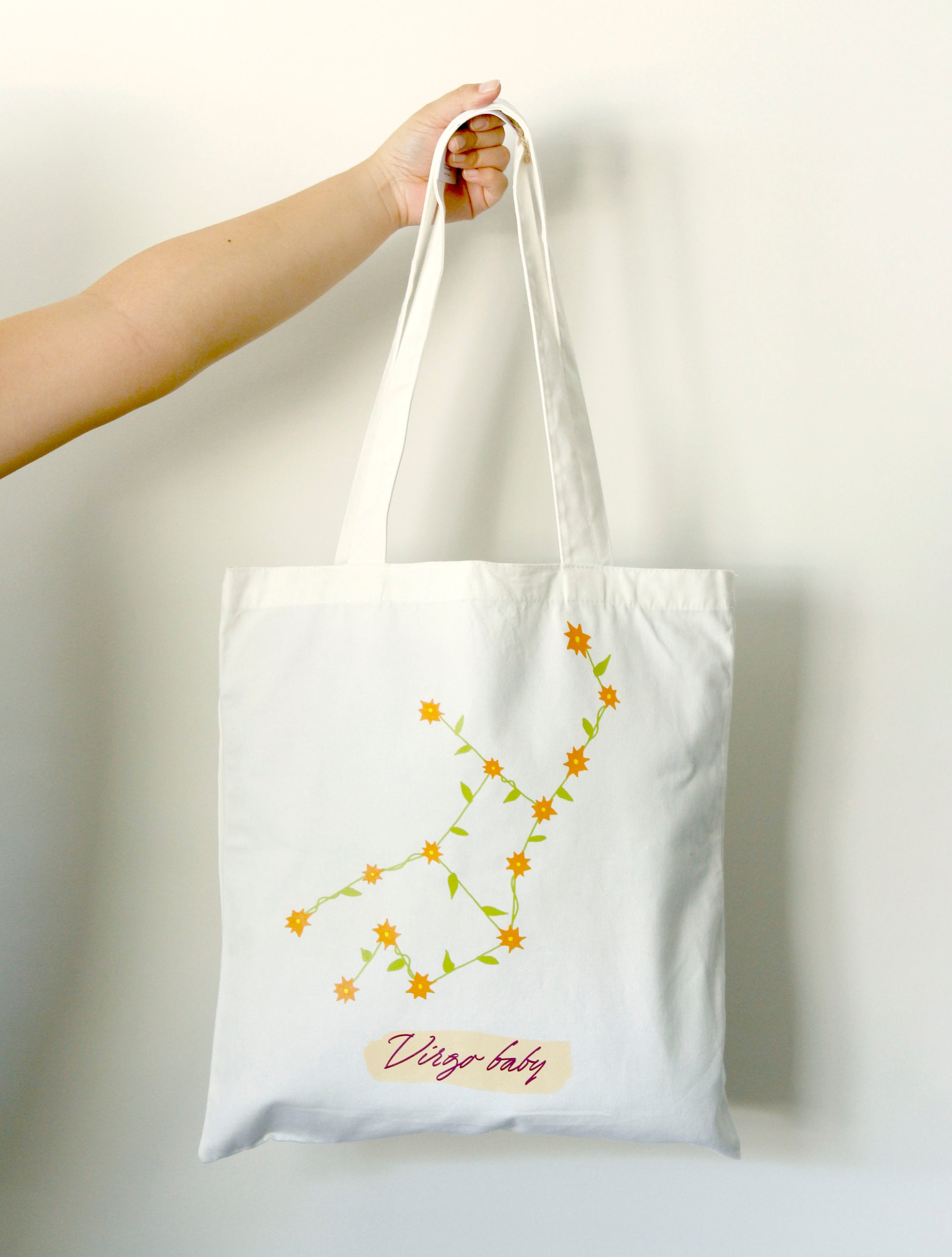 Tote bag with floral design and 'Virgo baby' text held by a hand on a white background